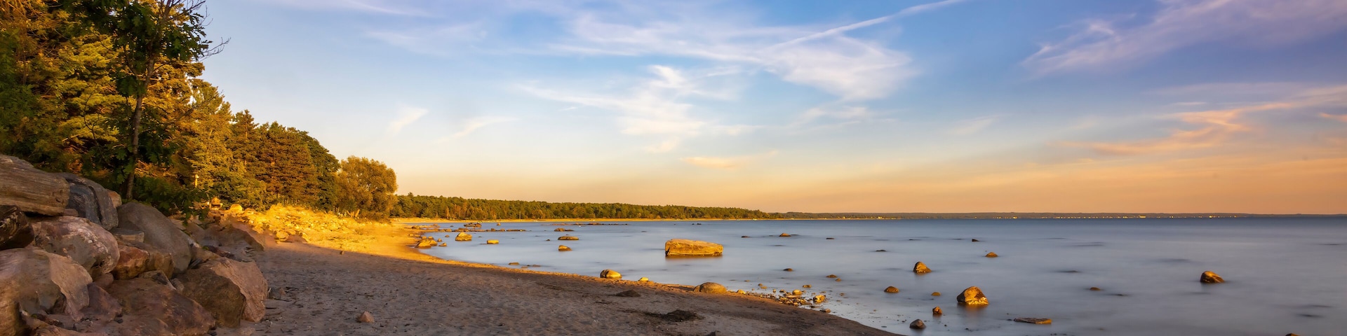 A stunning sunset over a serene beach in Tiny, Ontario, capturing the tranquil beauty and vibrant colors of the evening sky reflecting on the calm waters.