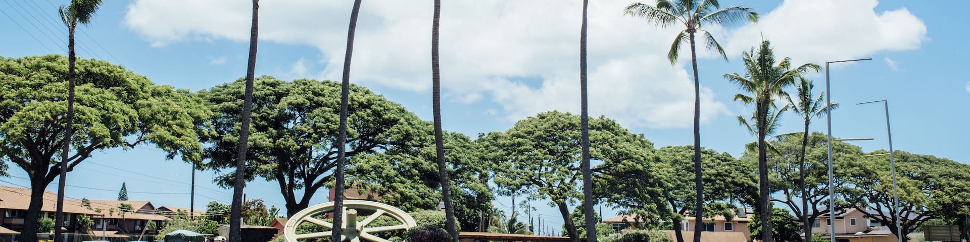 A sign welcoming visitors to Historic Ewa Villages with palm trees and houses in the background.