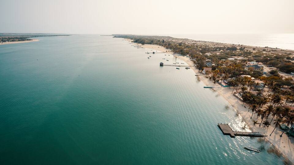 An aerial view of a coastal area with a beach, palm trees, and a pier extending into the water.