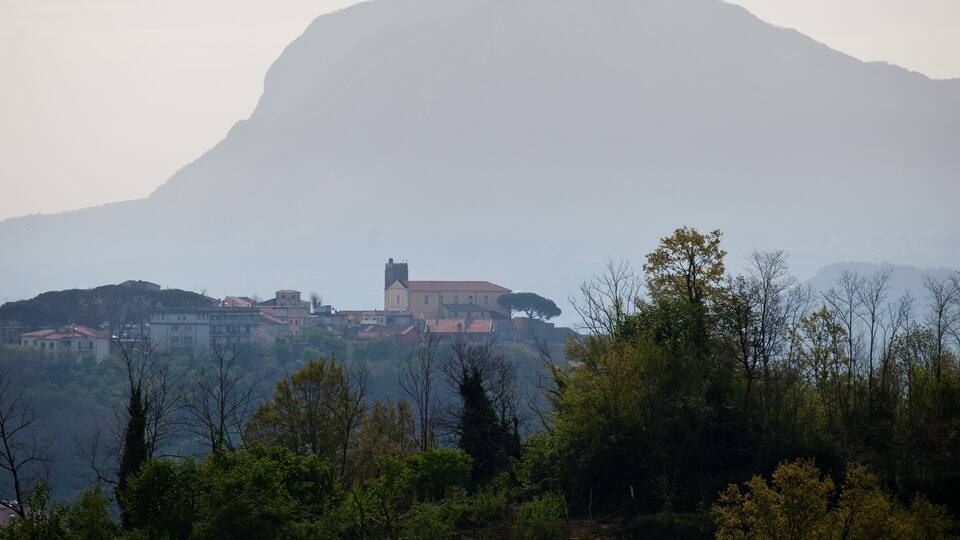 A mountain with a church on a hill, surrounded by trees and buildings.