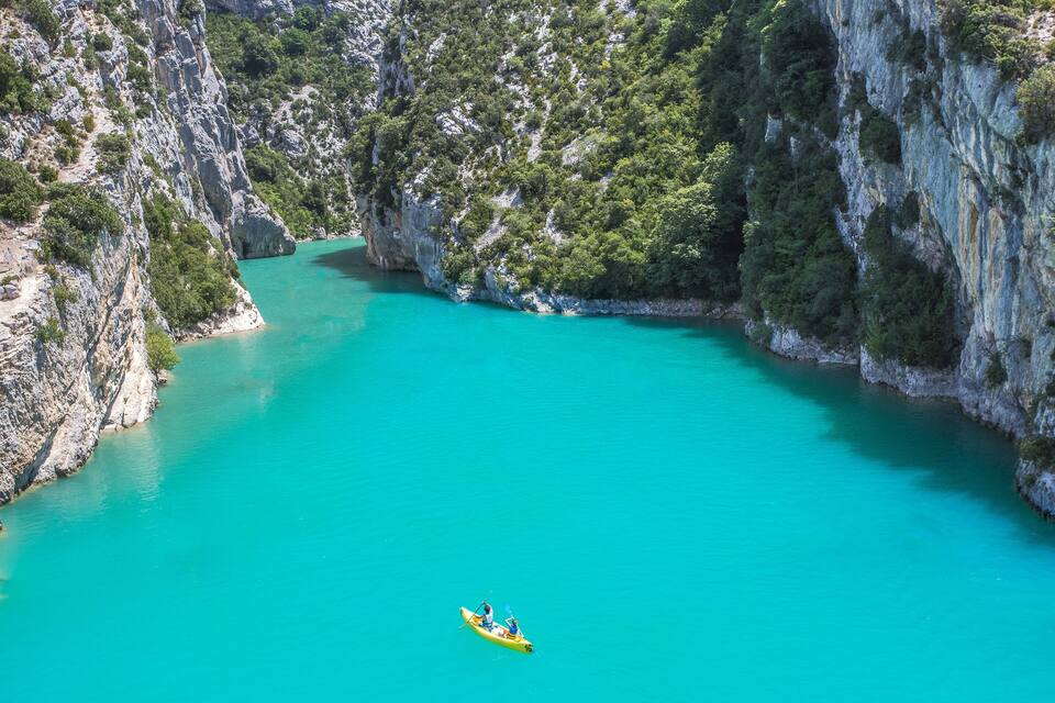 A kayaker in a yellow kayak on a turquoise river surrounded by rocky cliffs and dense greenery.
