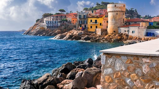 Perfect tiny seaside village of "Giglio Porto" with multi colored houses, an ancient defensive tower and a rocky coastline against a deep blue Mediterranean sea. - Giglio Island, Tuscany, Italy