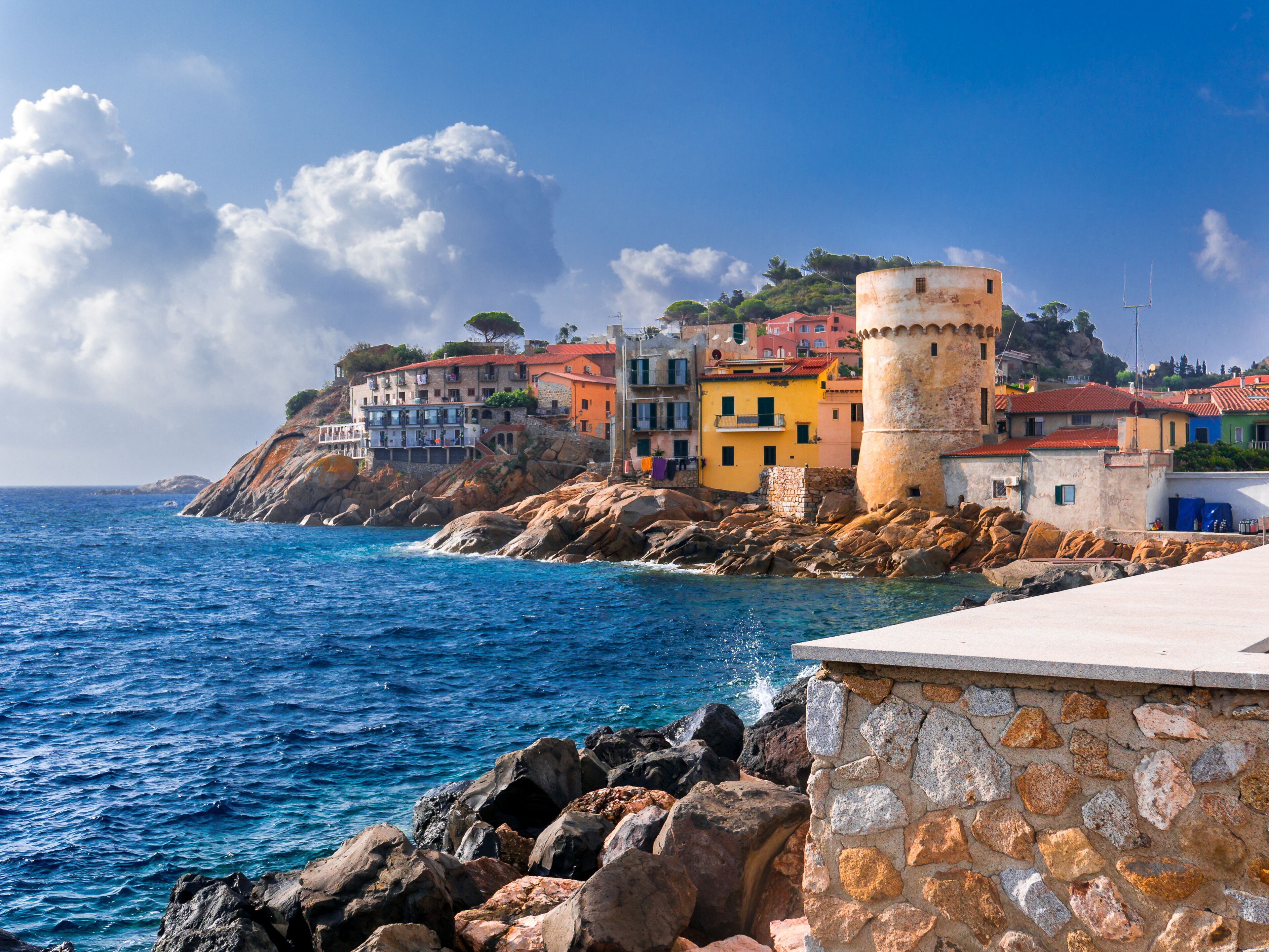 A coastal town with colorful buildings, a prominent tower, and rocky cliffs overlooking the sea.