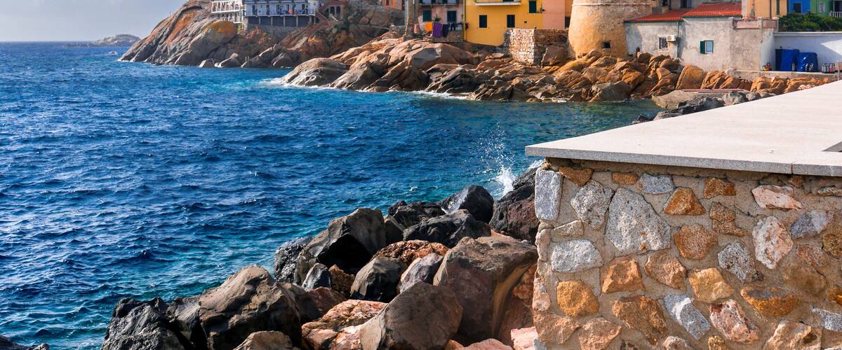 A coastal town with colorful buildings, a prominent tower, and rocky cliffs overlooking the sea.
