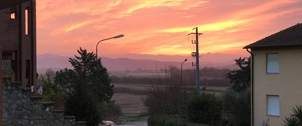 A sunset over a rural landscape with a house, street lamp, and distant mountains.
