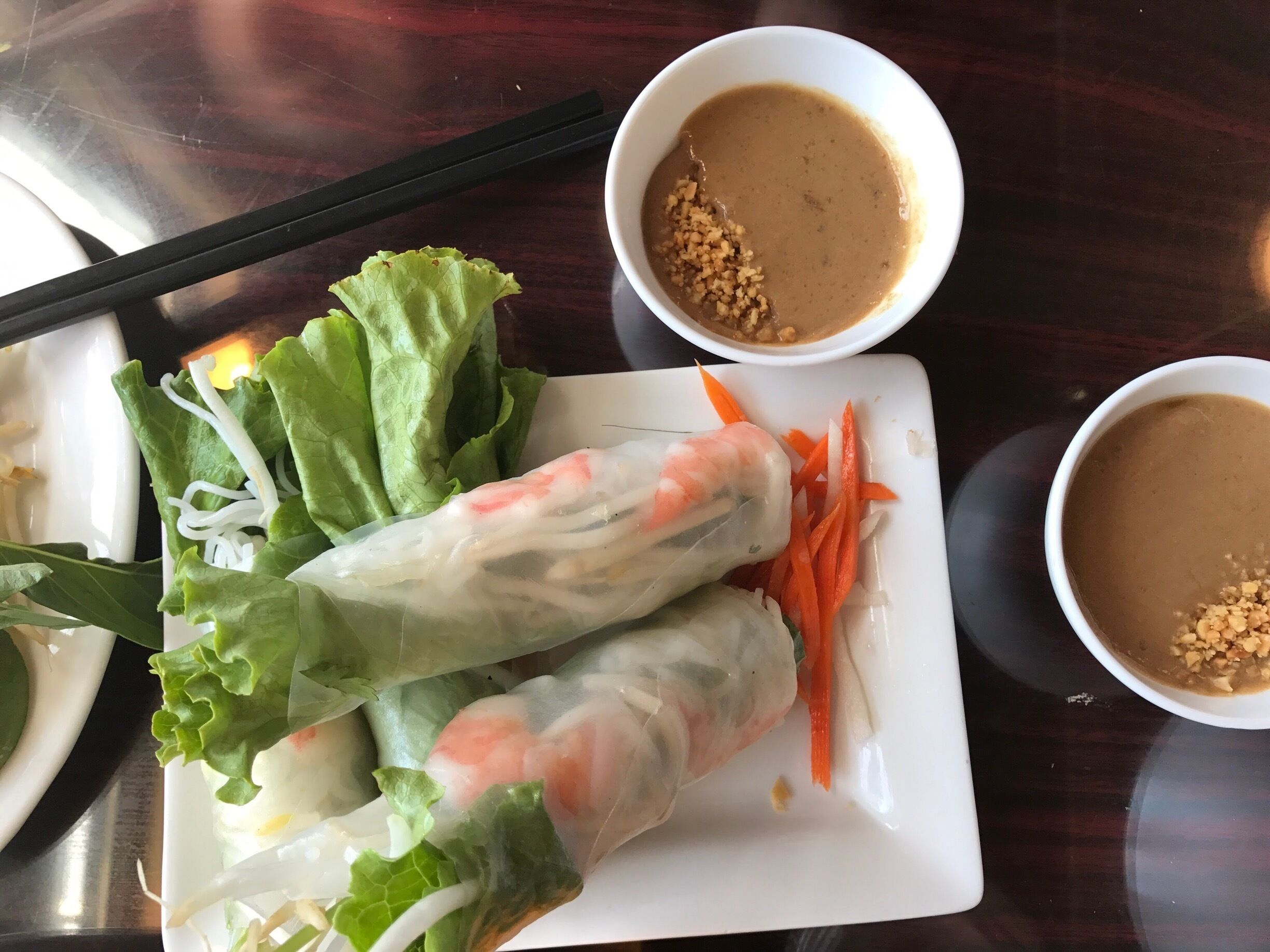 A plate of Vietnamese spring rolls with lettuce, carrots, and shrimp, accompanied by two small bowls of peanut sauce.