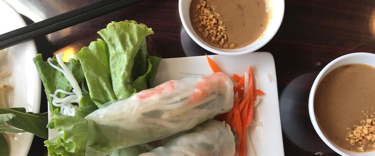 A plate of Vietnamese spring rolls with lettuce, carrots, and shrimp, accompanied by two small bowls of peanut sauce.