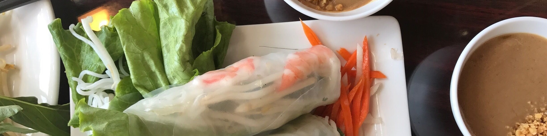 A plate of Vietnamese spring rolls with lettuce, carrots, and shrimp, accompanied by two small bowls of peanut sauce.