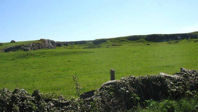 Un campo verde con un muro de piedra y afloramientos rocosos.