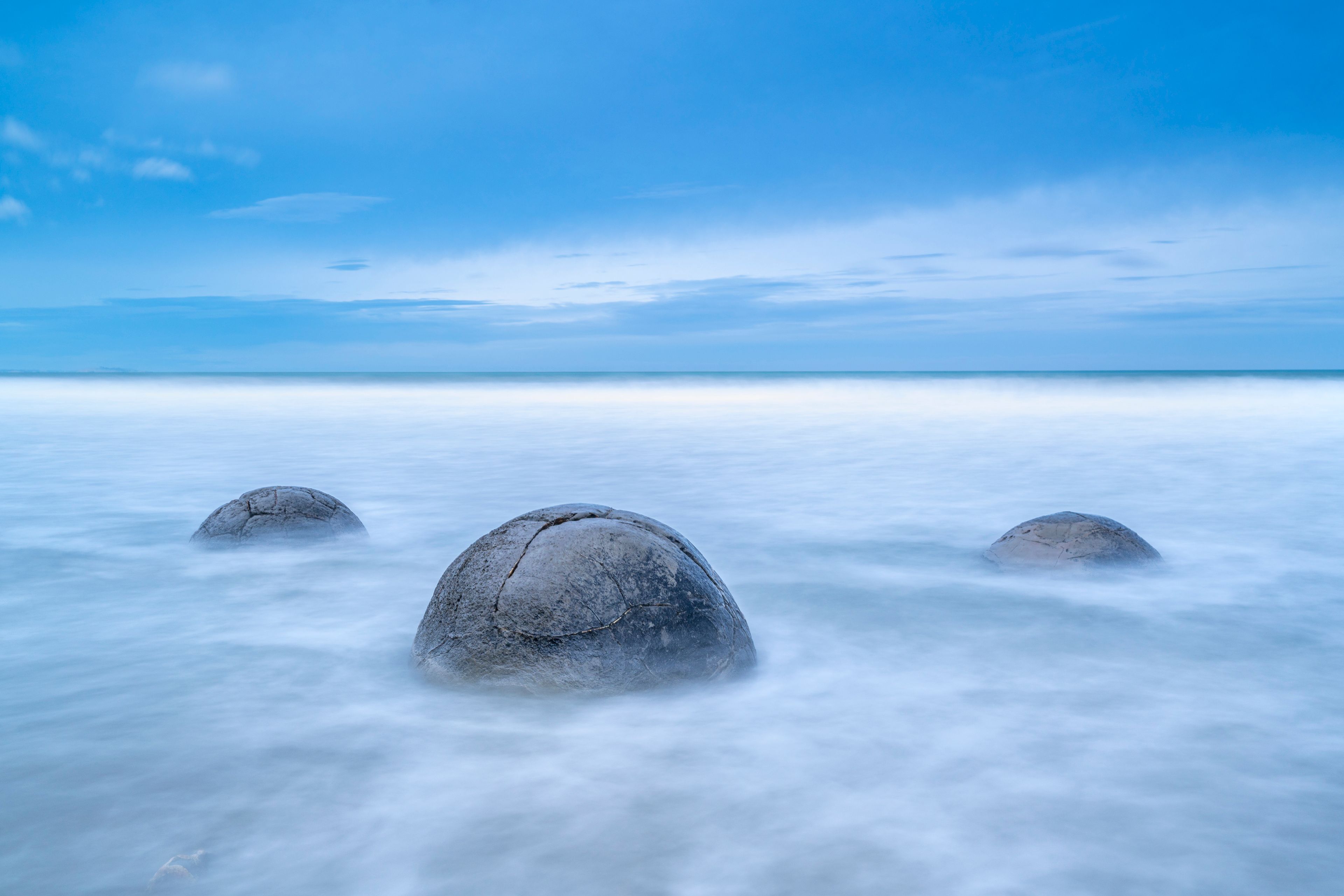 A calm sea with three large rocks in the foreground and a clear sky.