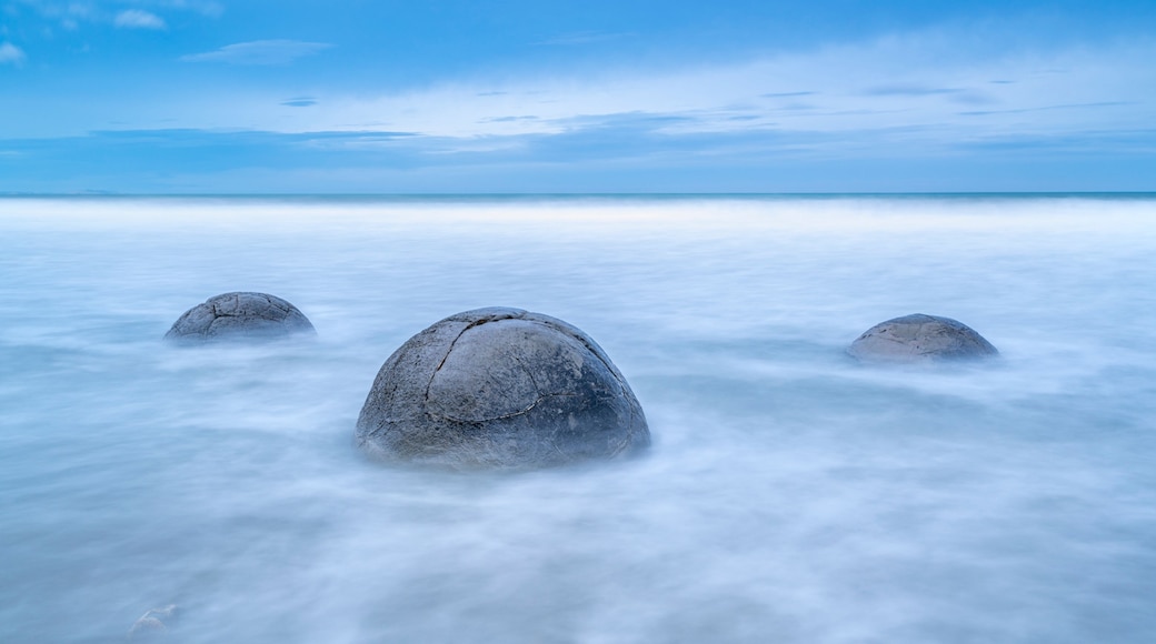 A calm sea with three large rocks in the foreground and a clear sky.
