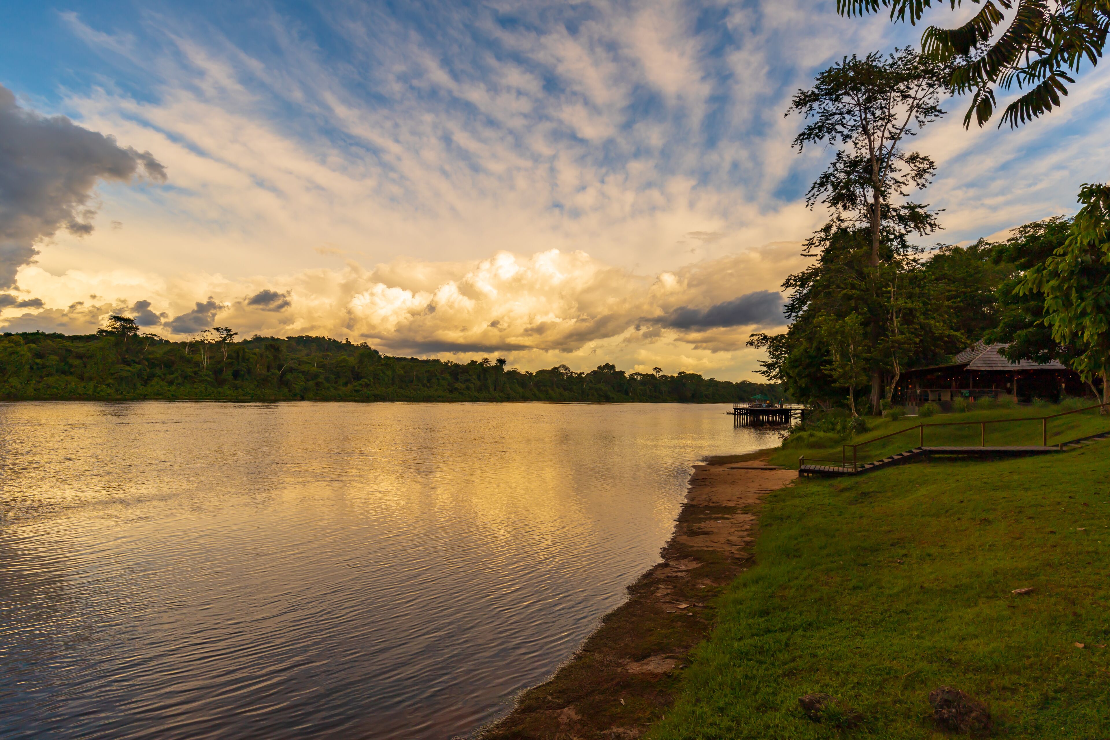 A calm lake with a dock, grassy banks, and a forested hill in the background.