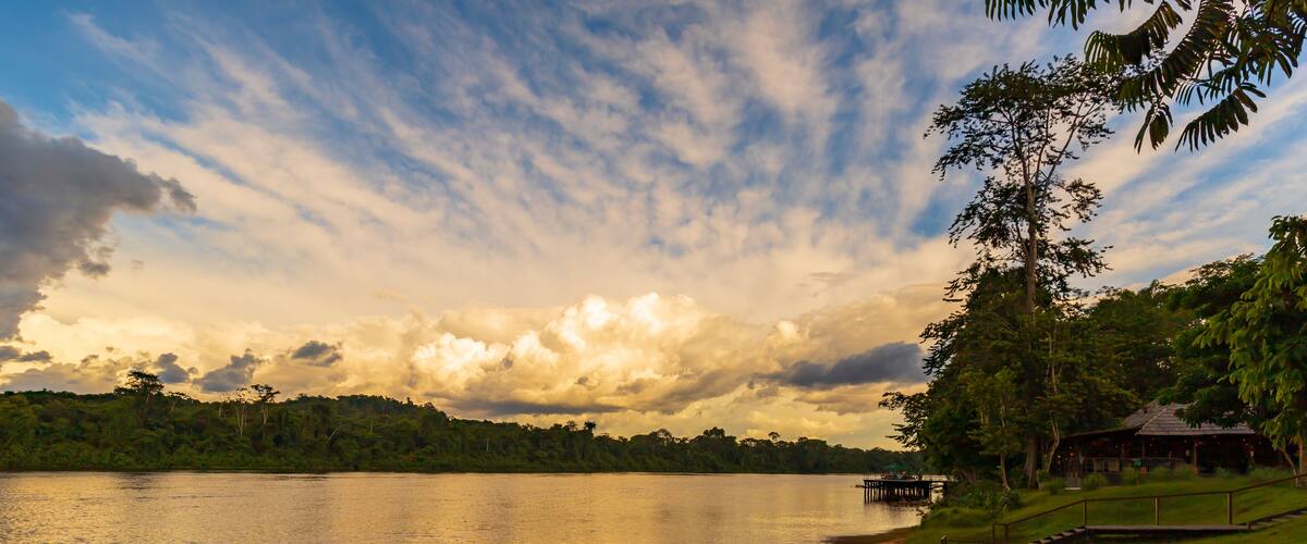 A calm lake with a dock, grassy banks, and a forested hill in the background.