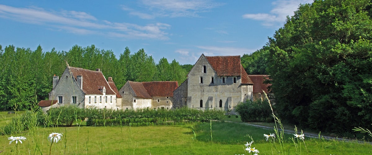 A historic stone building with a red roof, surrounded by lush greenery and white flowers.