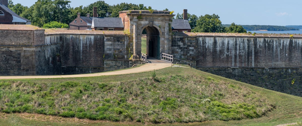A historic stone fort with a central archway, surrounded by greenery and a clear sky.