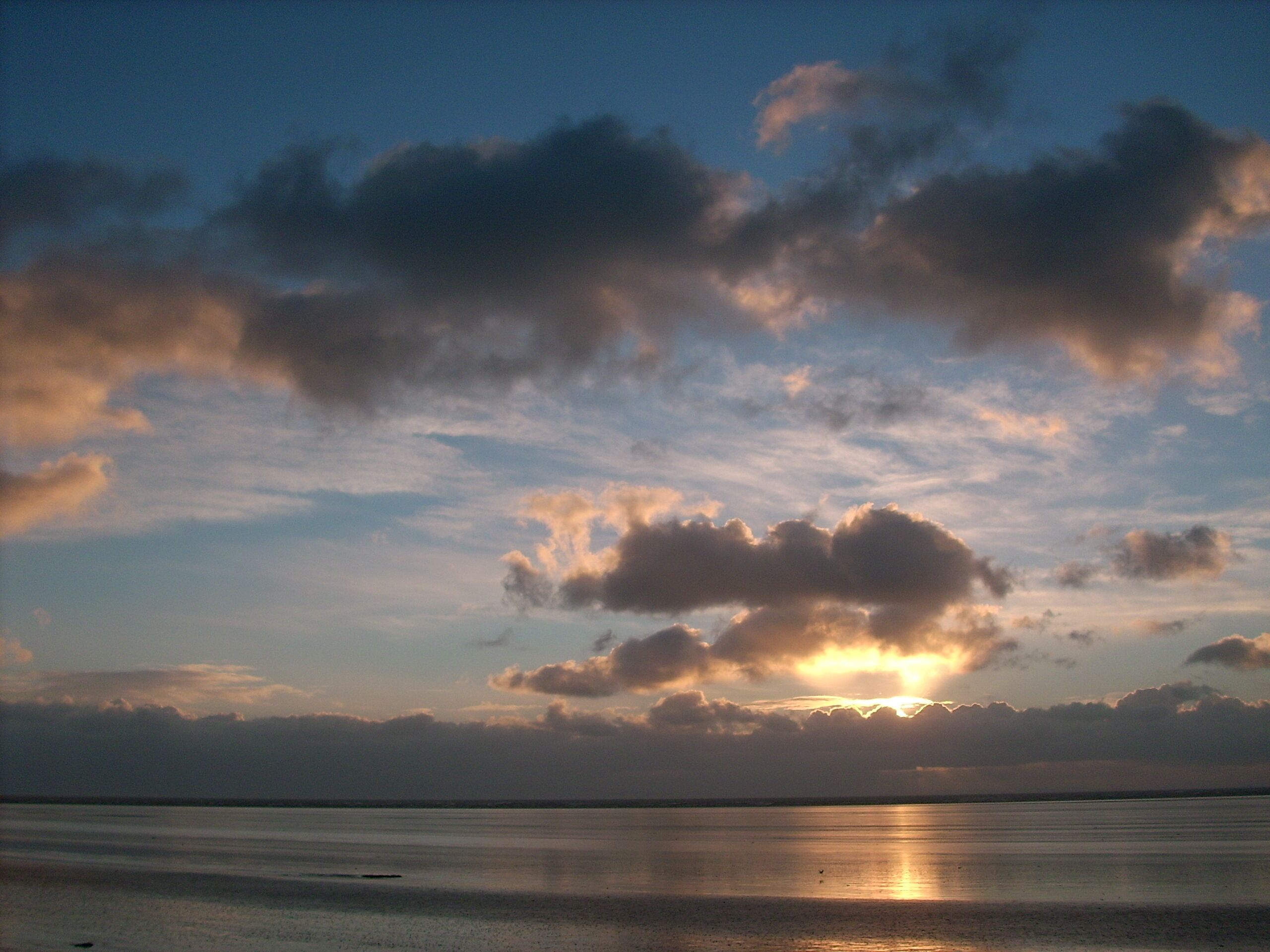 A sunset over a calm sea with scattered clouds.