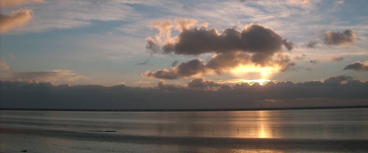 A sunset over a calm sea with scattered clouds.