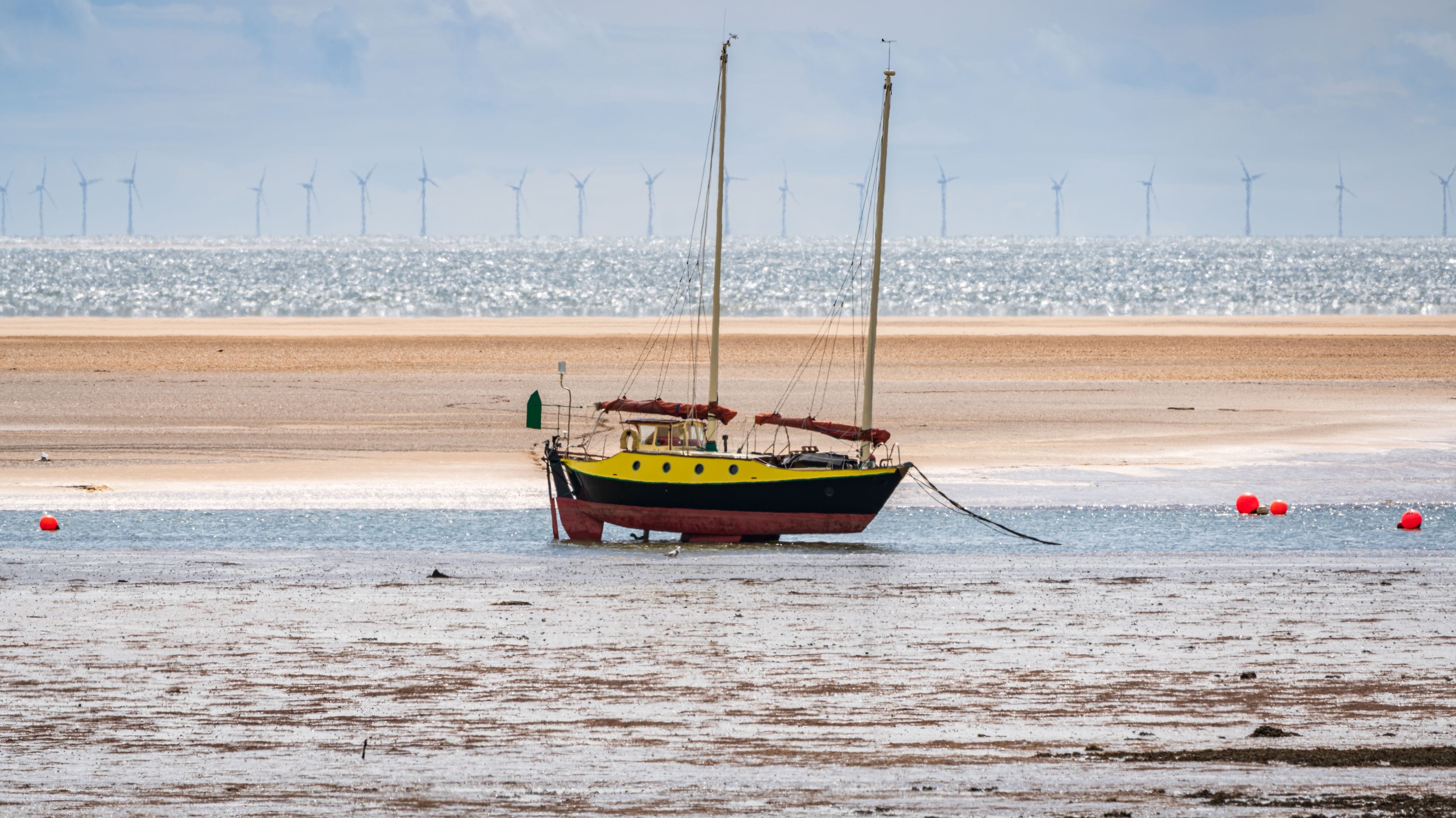 A sailboat on a sandy beach with wind turbines in the background.