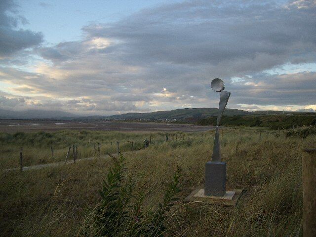 A grassy field with a metal sculpture and a distant view of hills.