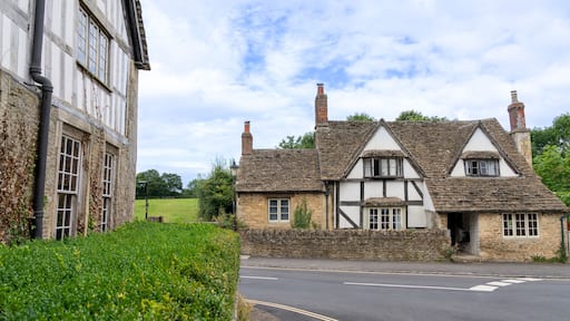 A traditional half-timbered house with a stone chimney, a paved road, and a hedge in the foreground.