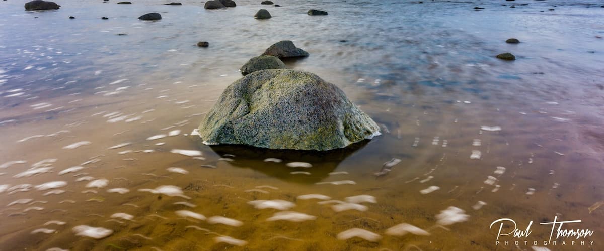 A rocky shoreline with clear water and a cloudy sky.