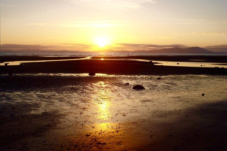 A sunset over a beach with wet sand and distant mountains.