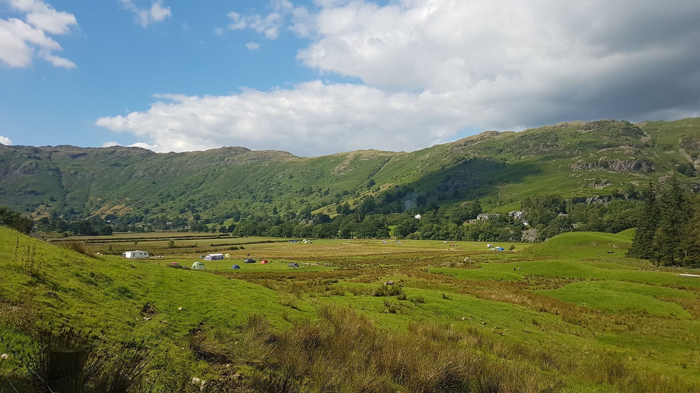 A lush green valley with rolling hills, a clear sky, and scattered buildings.