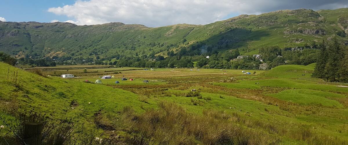 A lush green valley with rolling hills, a clear sky, and scattered buildings.