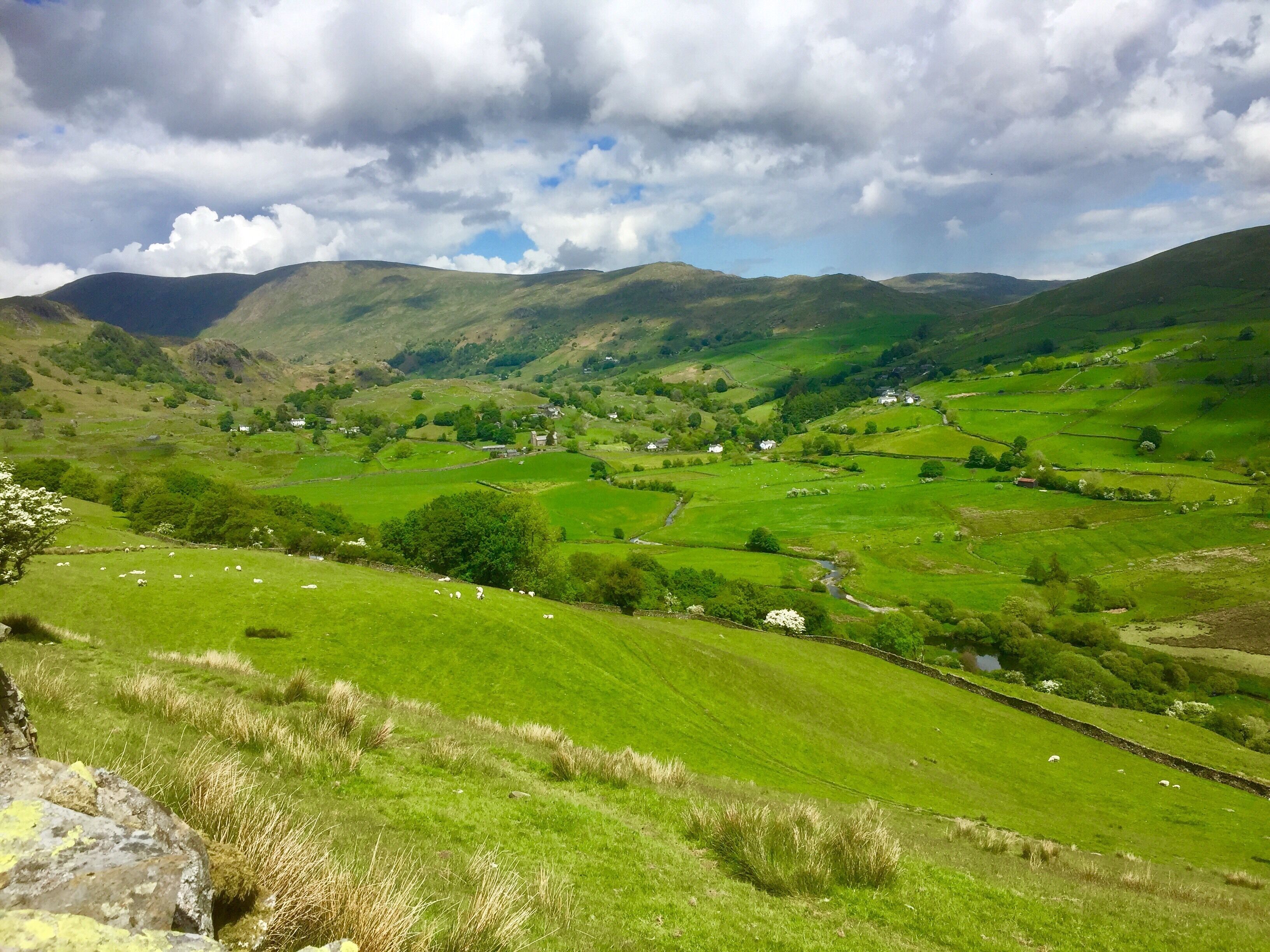 A lush green valley with rolling hills, scattered houses, and a river.