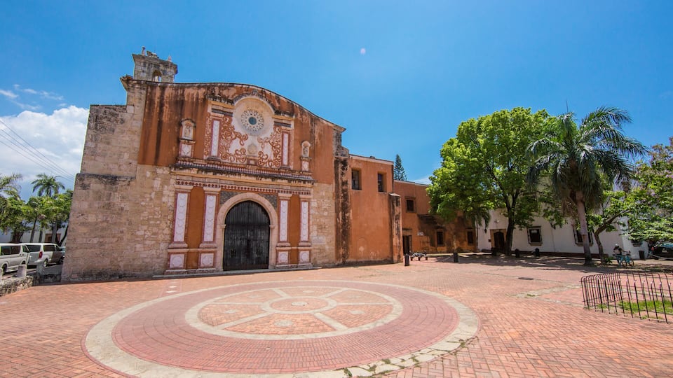 A historic building with a circular plaza, palm trees, and a clear blue sky.