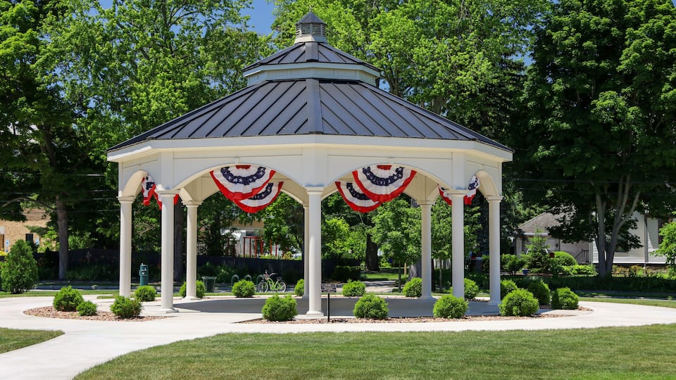 A gazebo with American flag decorations, surrounded by a well-maintained lawn and trees.