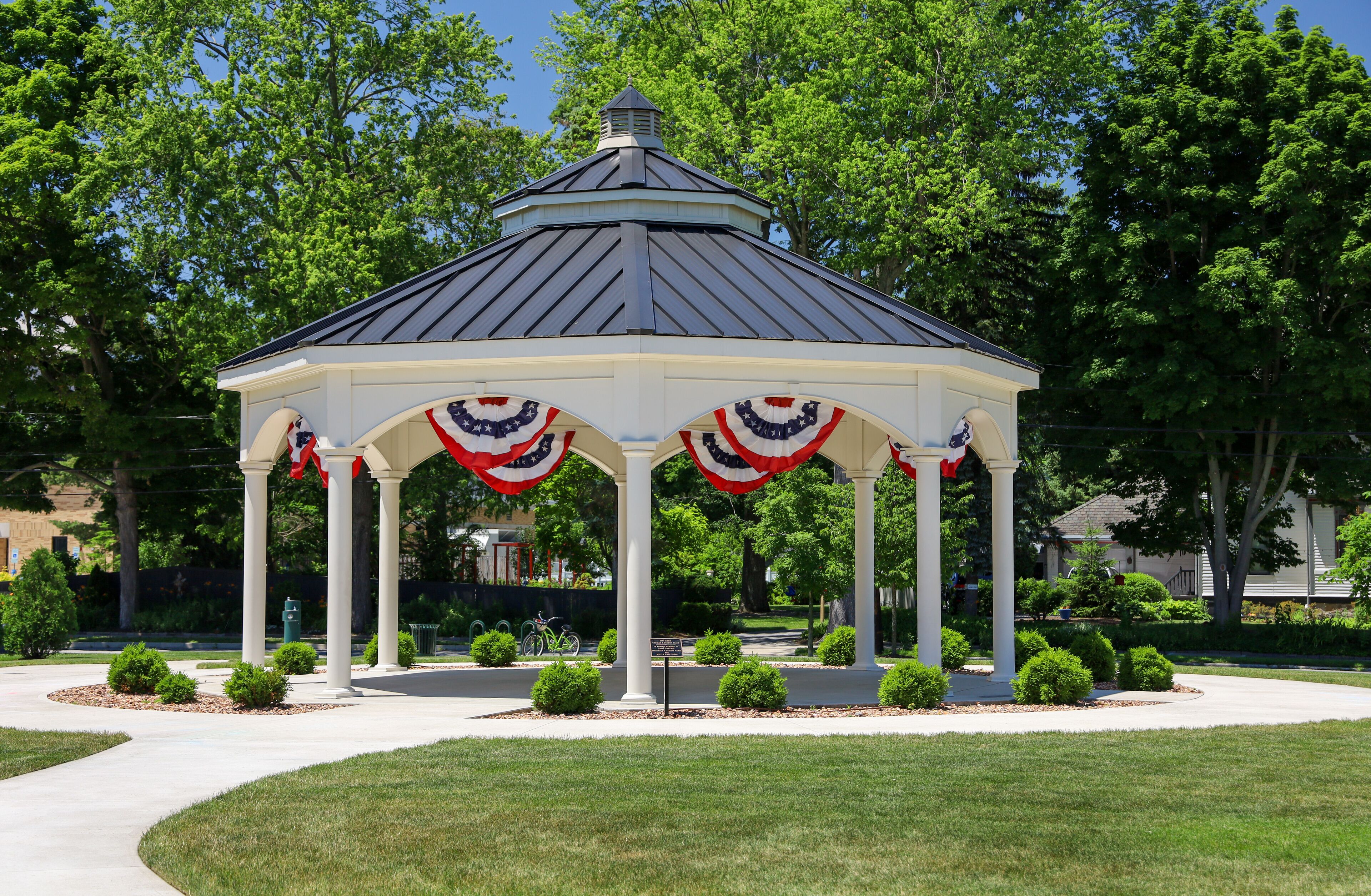 A gazebo with American flag decorations, surrounded by a well-maintained lawn and trees.