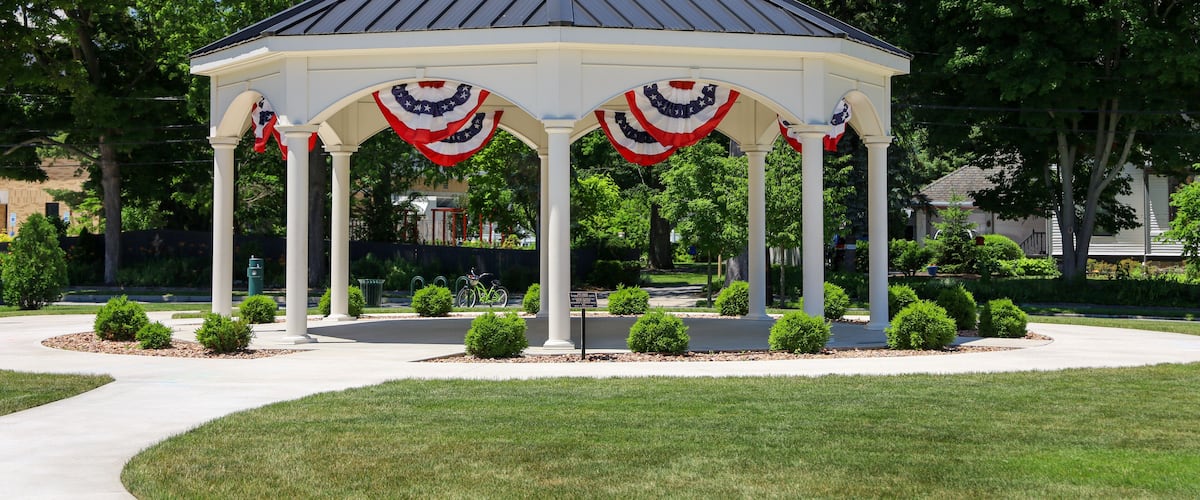 A gazebo with American flag decorations, surrounded by a well-maintained lawn and trees.
