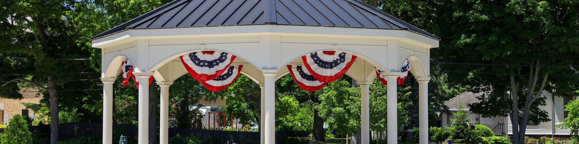 A gazebo with American flag decorations, surrounded by a well-maintained lawn and trees.