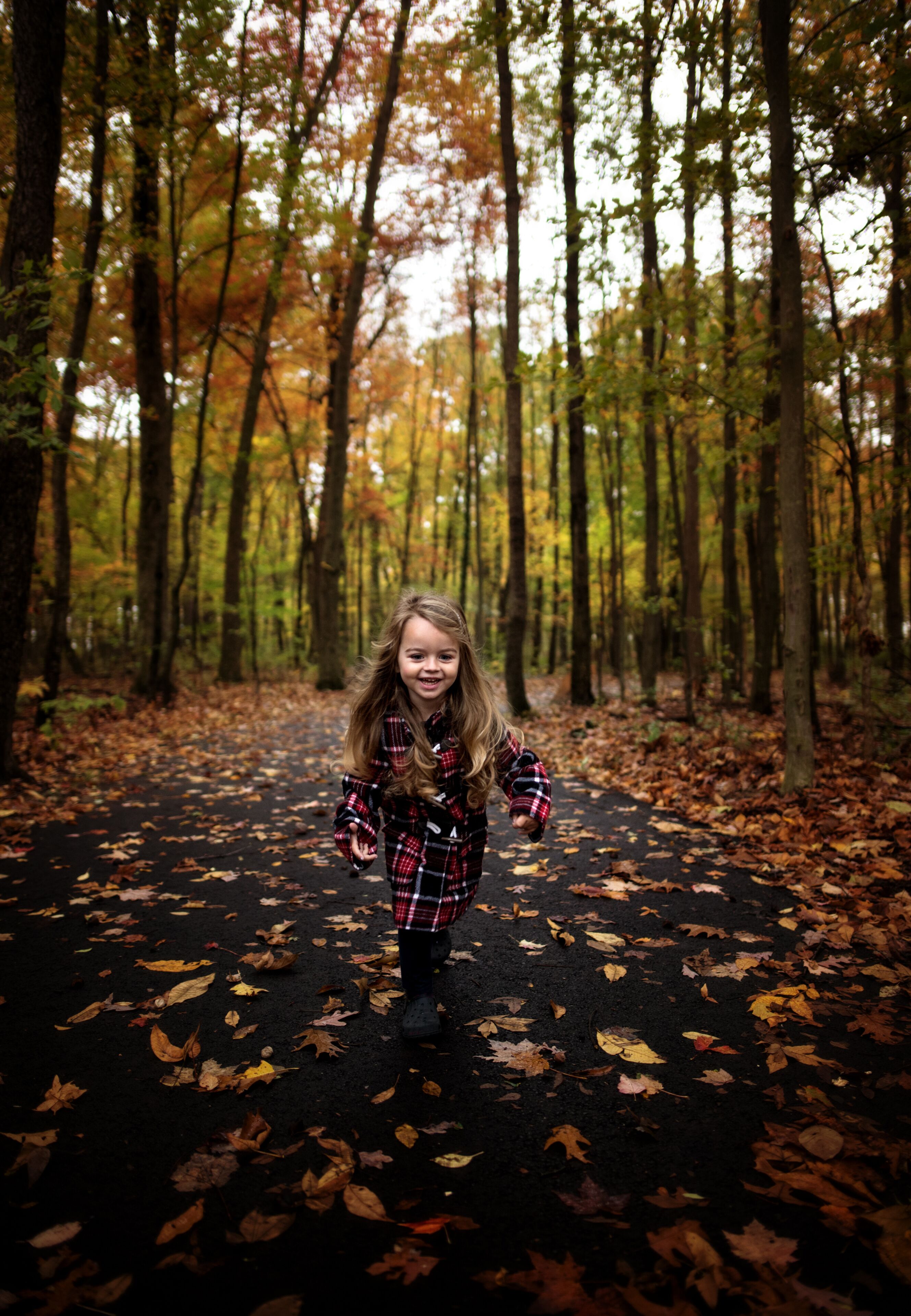 Happy young girl running down path with colorful leaves and trees