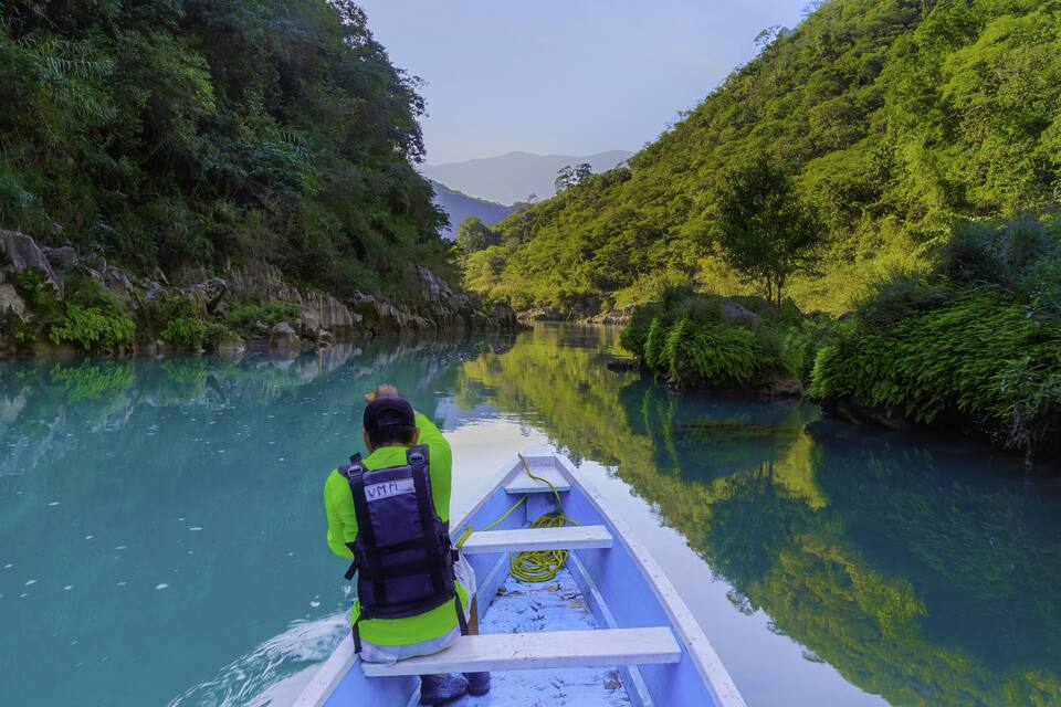 Una persona en kayak en un río tranquilo rodeado de vegetación exuberante y colinas.