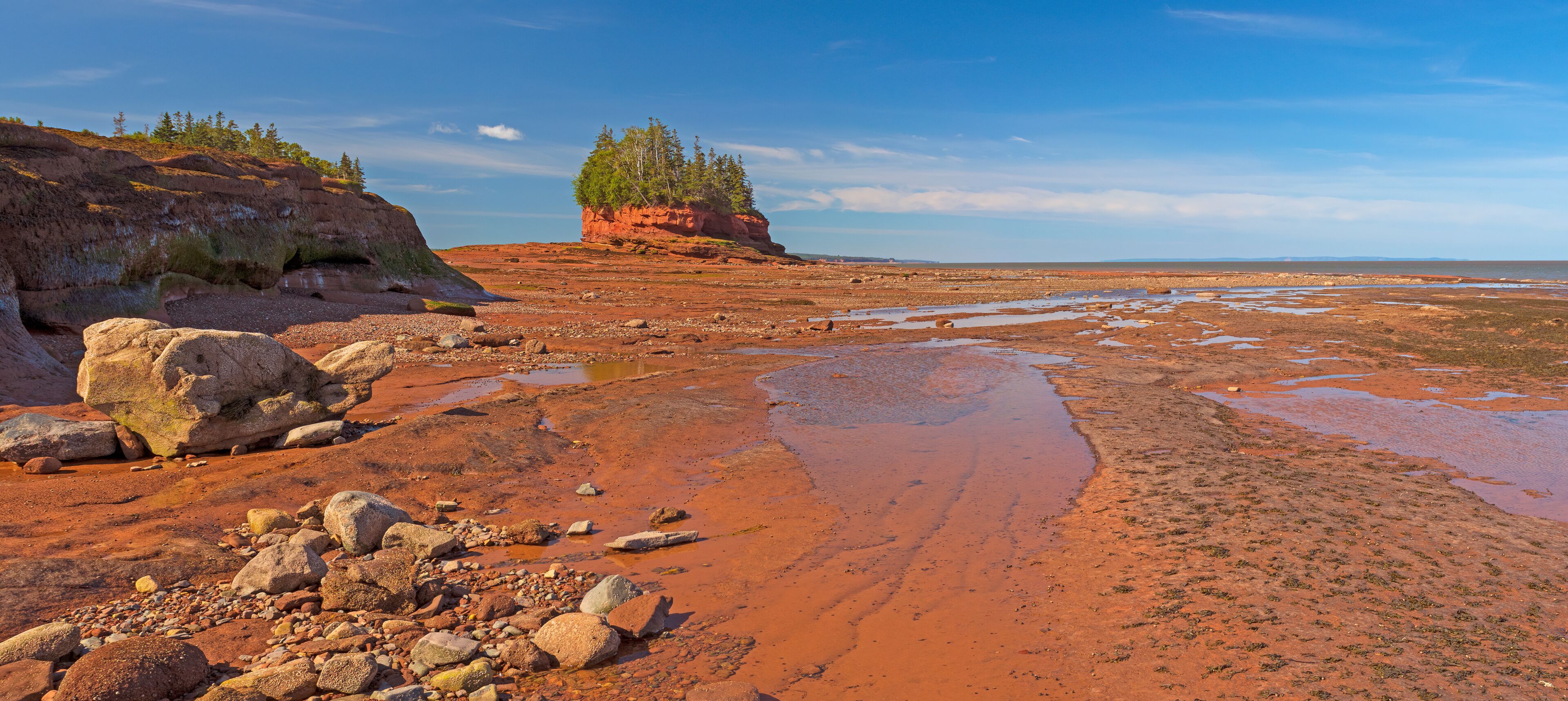 A red rock landscape with scattered boulders and a small cluster of trees on a hill.