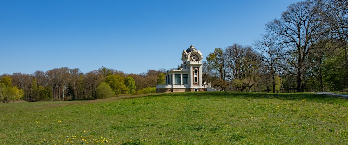 A historic building with a dome and columns in a grassy field with trees in the background.