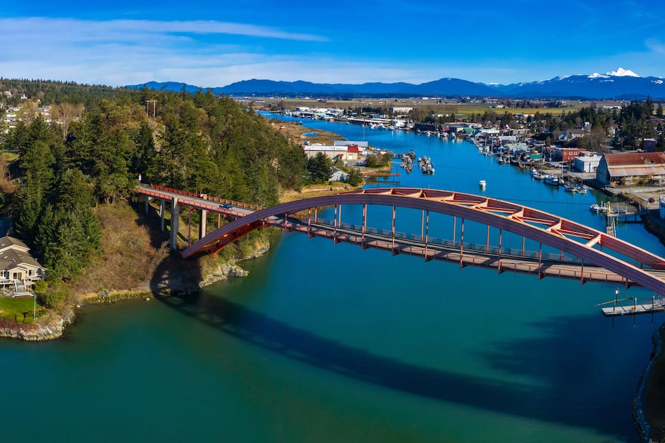 Un puente sobre un río, con un pueblo y montañas al fondo.