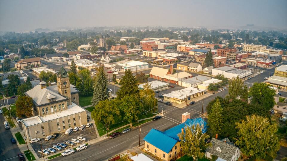 An aerial view of a town with a prominent church, a blue-roofed building, and a mix of commercial and residential structures.