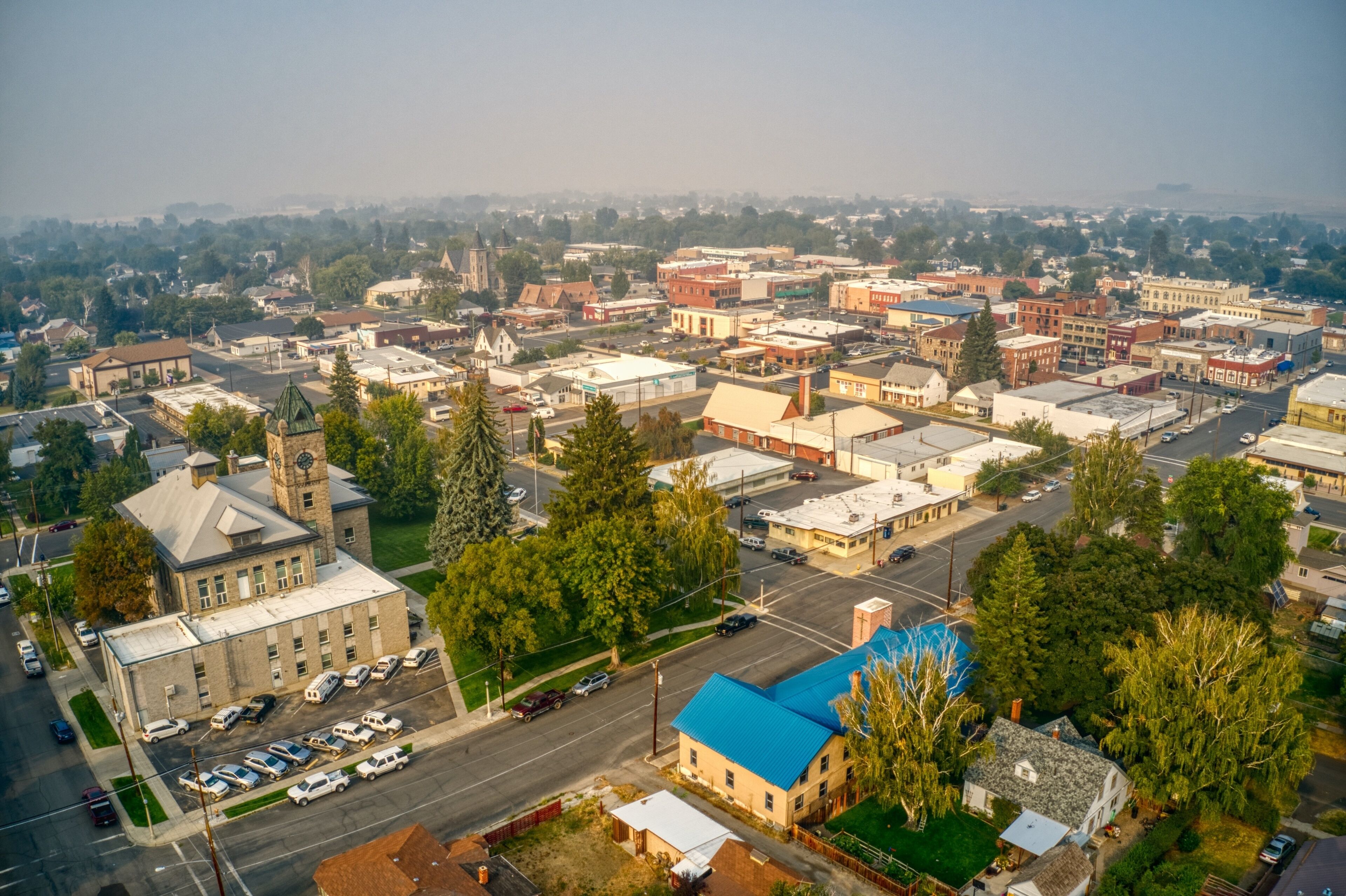 An aerial view of a town with a prominent church, a blue-roofed building, and a mix of commercial and residential structures.