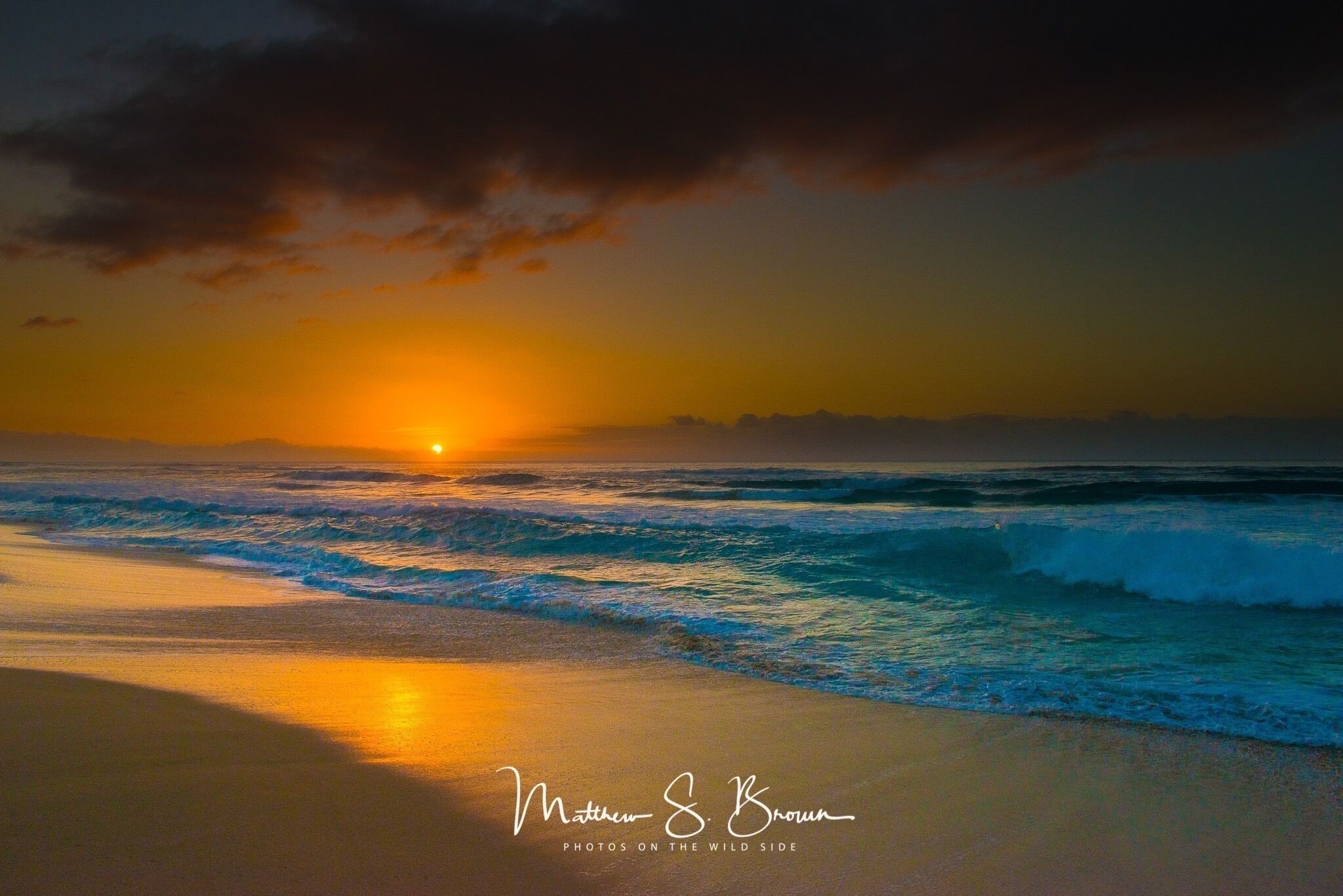 A sunset over the ocean with waves crashing onto the shore.