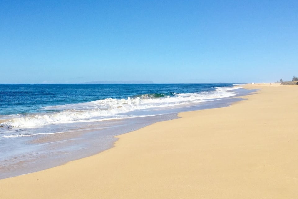 A wide sandy beach with gentle waves and a clear blue sky.