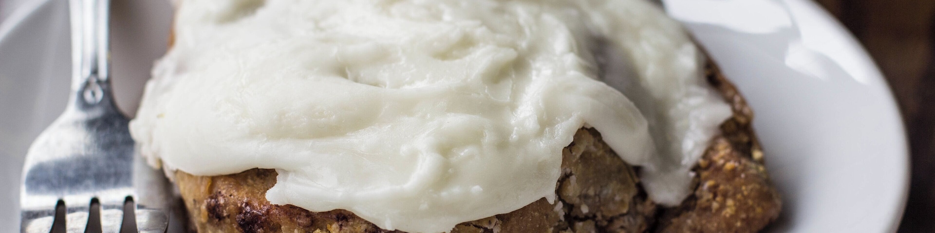 A slice of cake with white frosting on a plate.