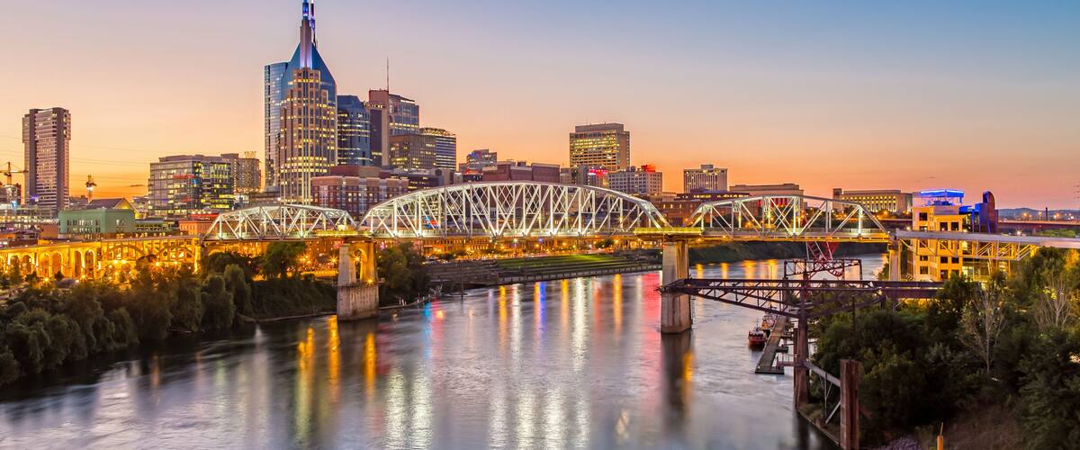 Un horizonte urbano al atardecer con un puente destacado que cruza un río, reflejando las luces de la ciudad.