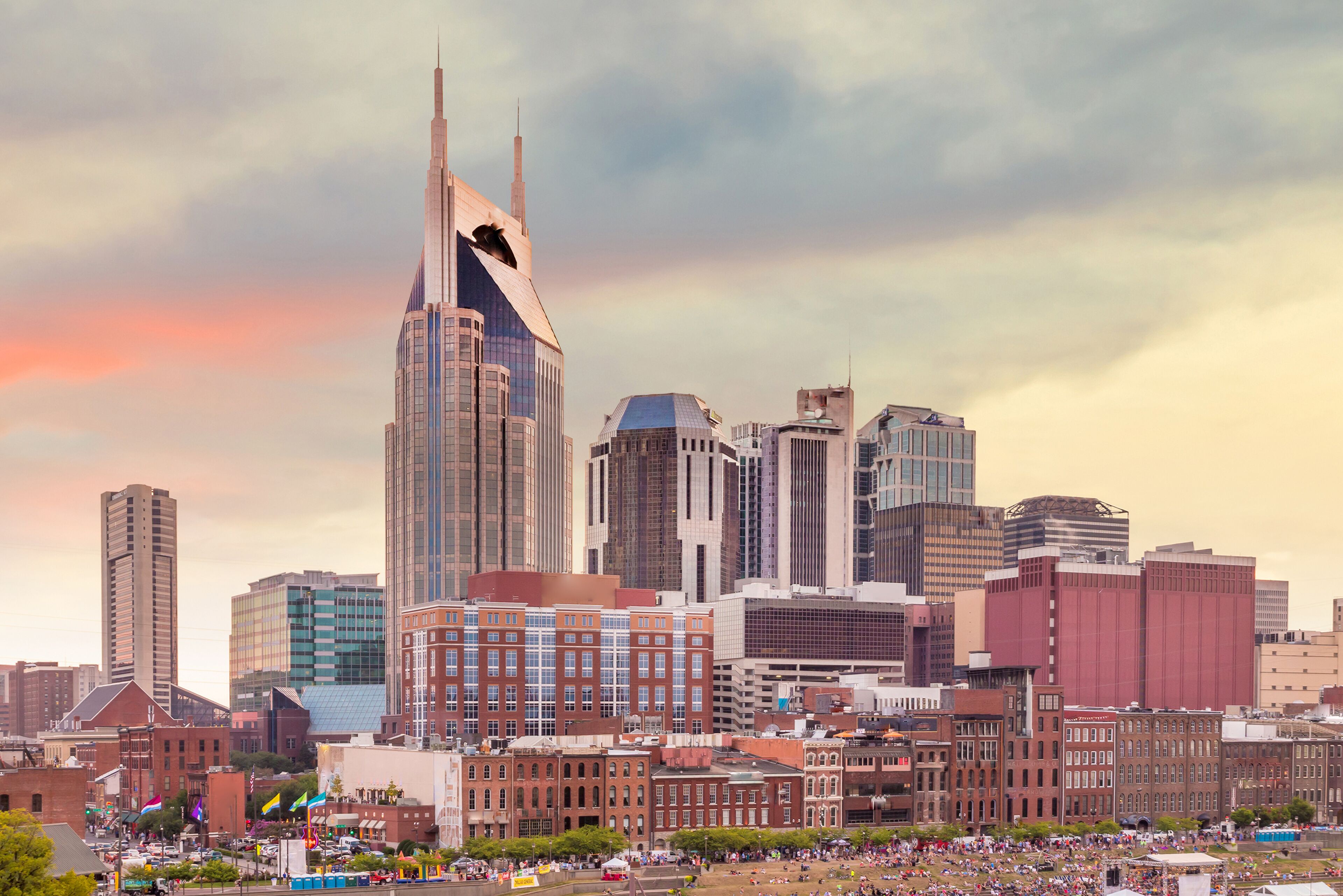 A city skyline with a prominent skyscraper, a mix of modern and historic buildings, and a crowded public space.