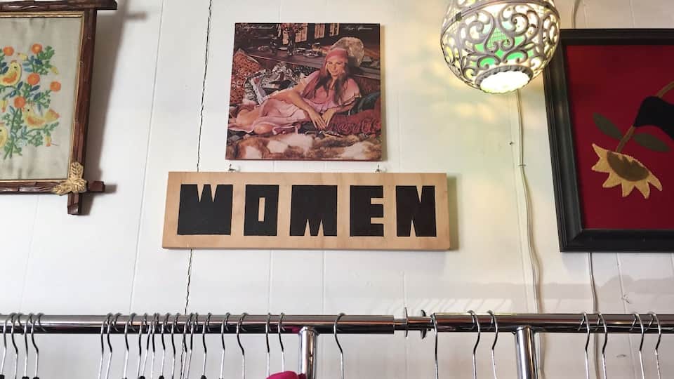 Eine Wand mit einem gerahmten Bild, einer Pendelleuchte und einem Schild mit der Aufschrift 'WOMEN'.