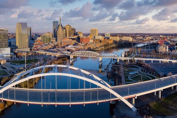 A cityscape with a prominent curved bridge over a river, surrounded by modern buildings and a clear sky.