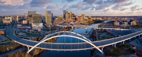 A cityscape with a prominent curved bridge over a river, surrounded by modern buildings and a clear sky.