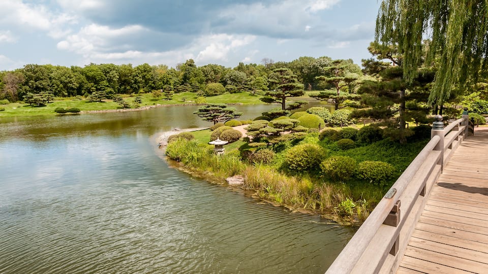 A wooden bridge over a calm river, surrounded by lush greenery and trees.